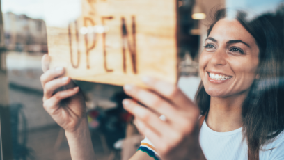 A woman hanging an open sign on the window of her business