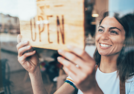 A woman hanging an open sign on the window of her business