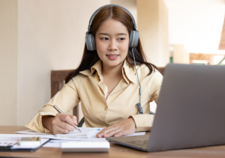 Woman wearing headphones while working on a laptop and writing notes