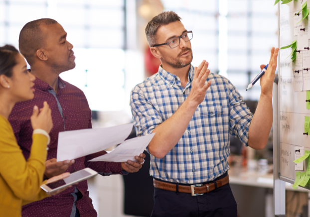 Instructor teaching a concept to two adult learners on a whiteboard