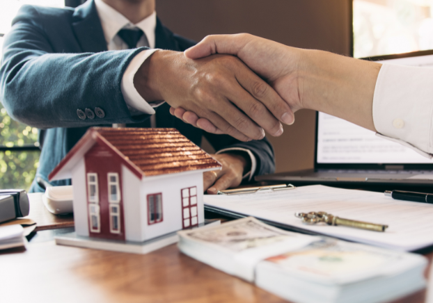 Two people shaking hands over small house display on table