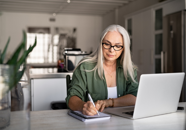 Woman writing in a notebook next to laptop