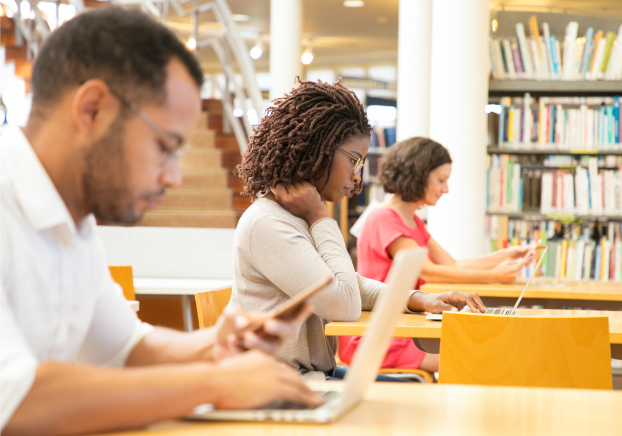 Individuals sitting in a library taking a test
